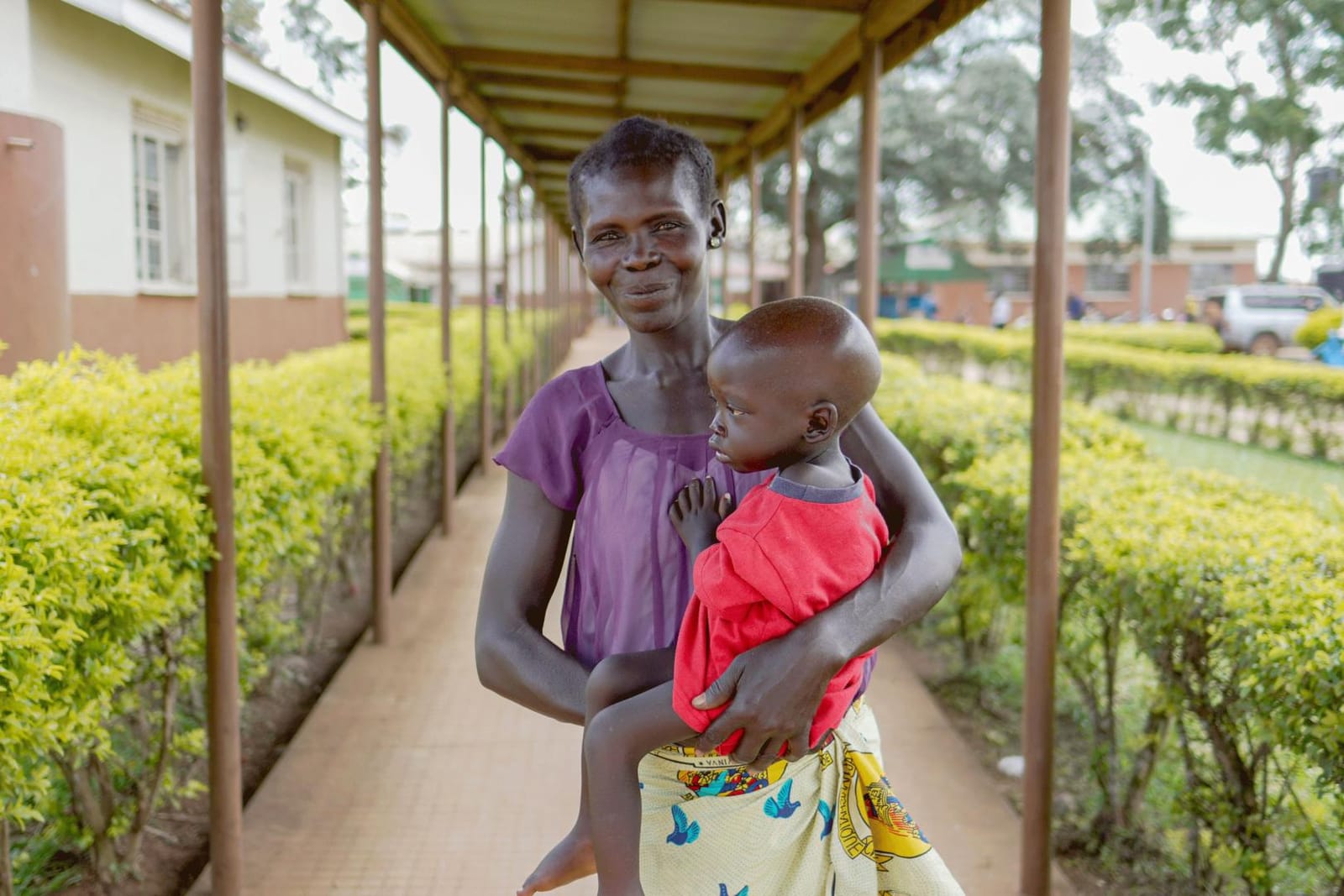 A mother carrying her young child along the covered walkway of a health centre in Koboko.