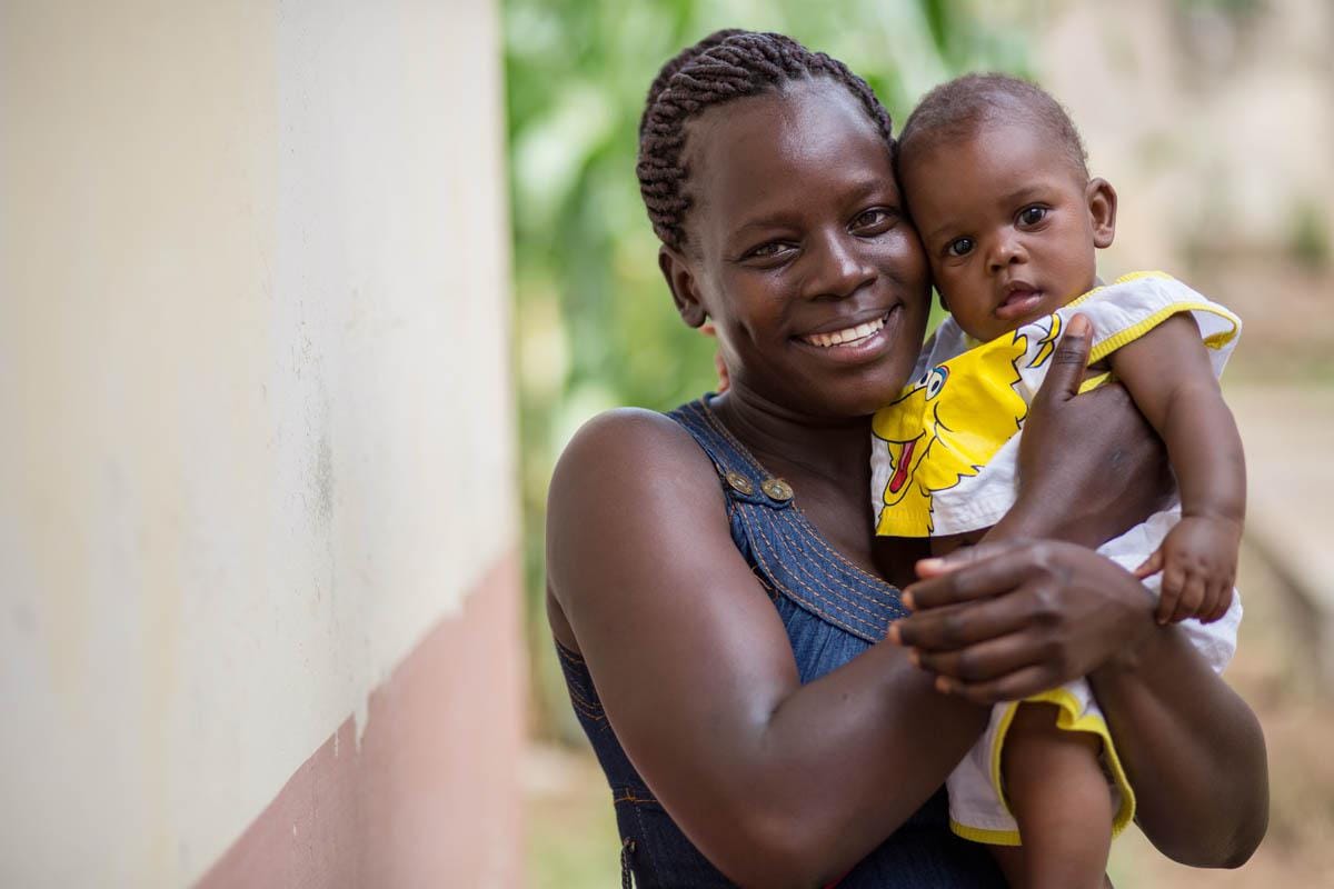 A mother holding her baby close outside a rural health post.
