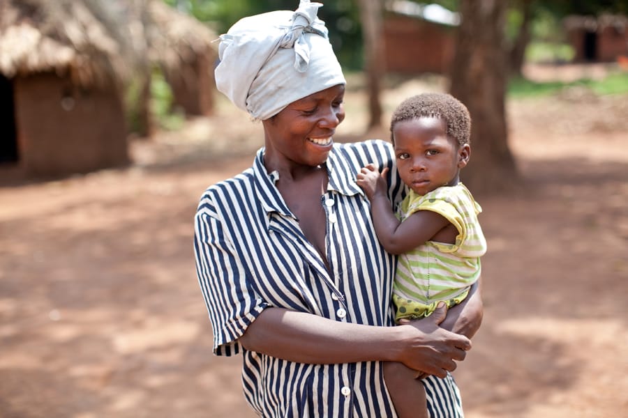 A mother carrying her young son outside their home in the village.