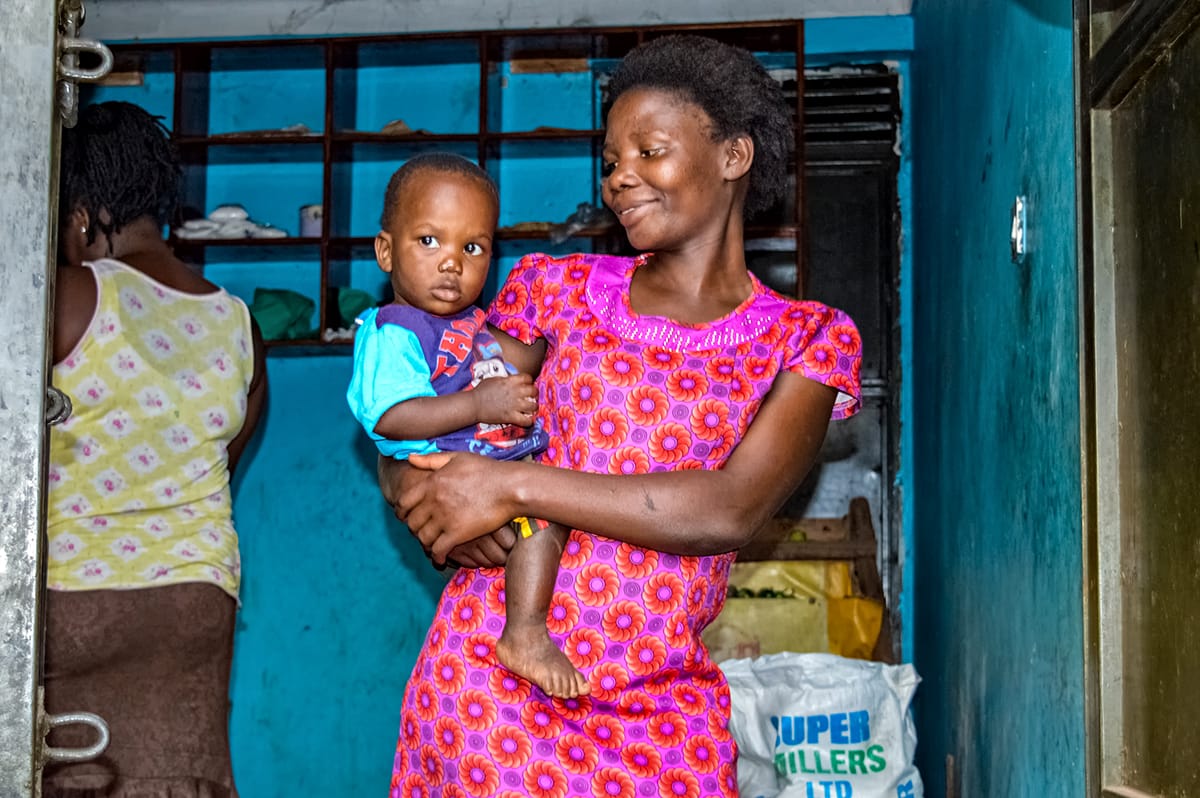 A mother holding her young son in the doorway of the small shop she runs.